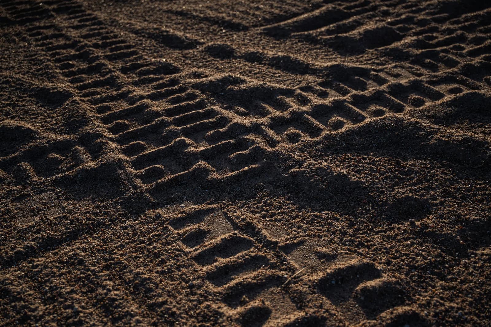 Equipment tire tracks pressed into the red earth in low raking light