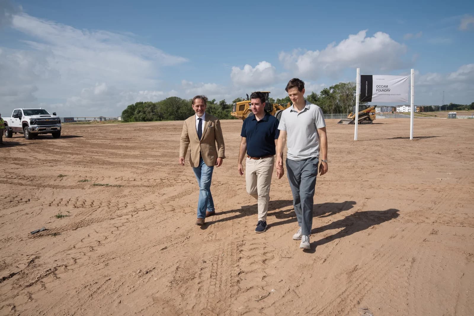 Three people walking the cleared site, equipment working behind them